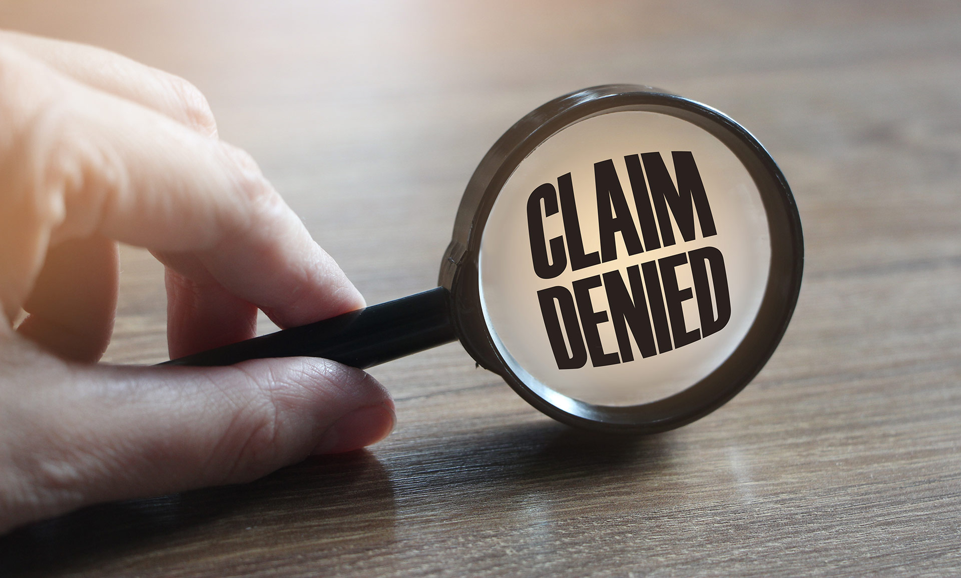 Hand holding a magnifying glass over text that says "Claim Denied"